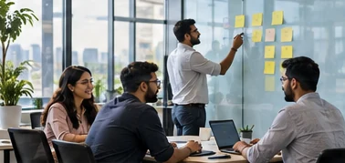 A small software team working around a long table in a bright office, one of them adding sticky notes to a glass wall